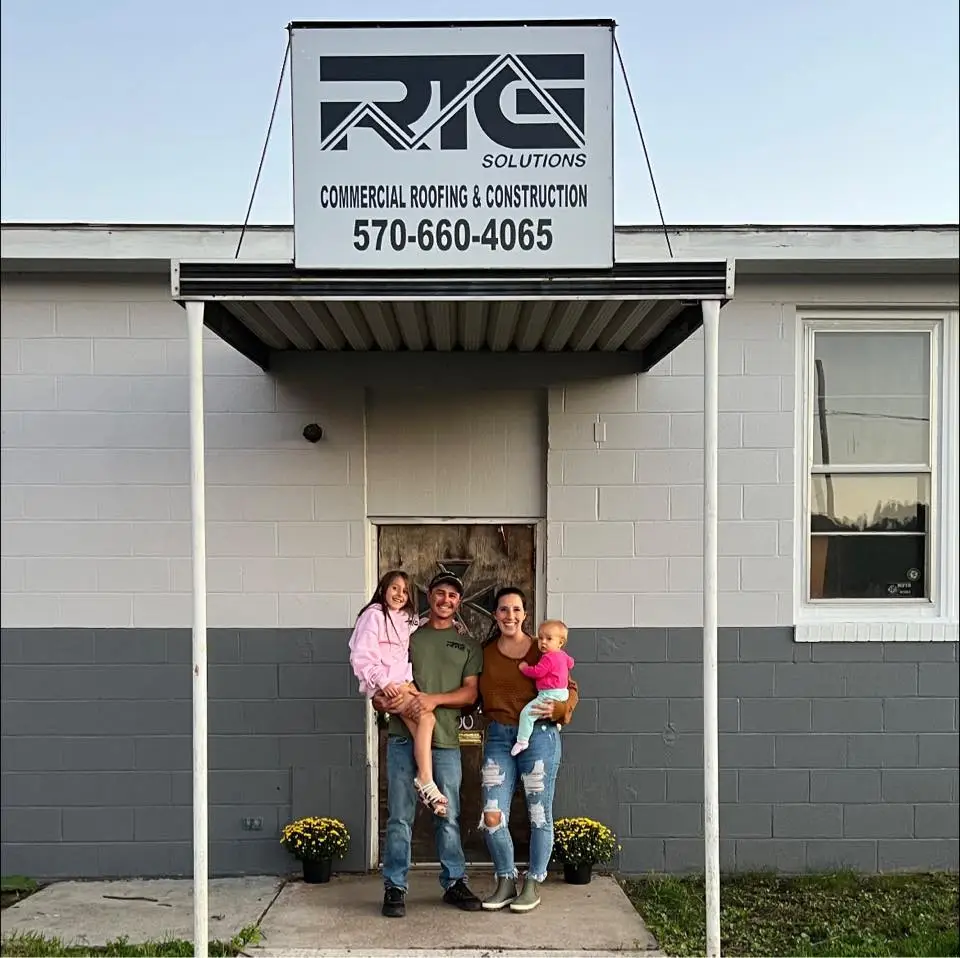 Hard Hats & Highlights | Commercial Roofing Contractors PA RTG Solutions President Sarah with her family under the company sign in Lock Haven, PA, representing a woman-owned commercial roofing business.