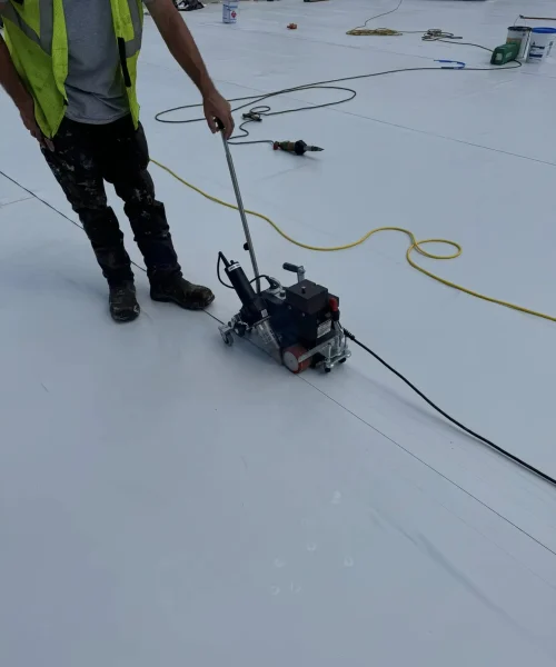 Roofer heat welding seams of single ply roofing system