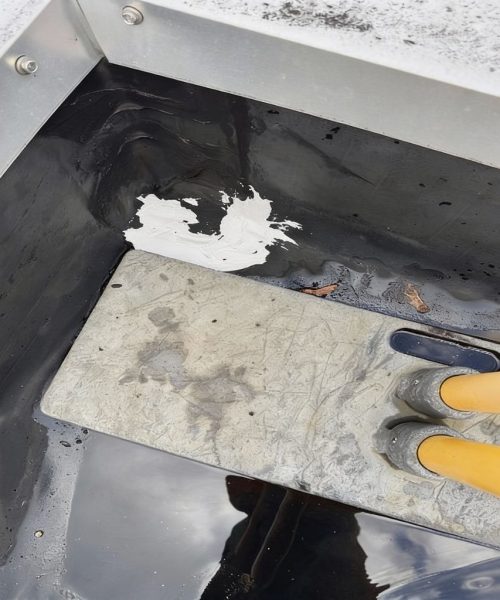 Patched corner tear on a commercial roof membrane at Park Hills Plaza, with sealant applied at the unit base flashing transition to stop leaks.