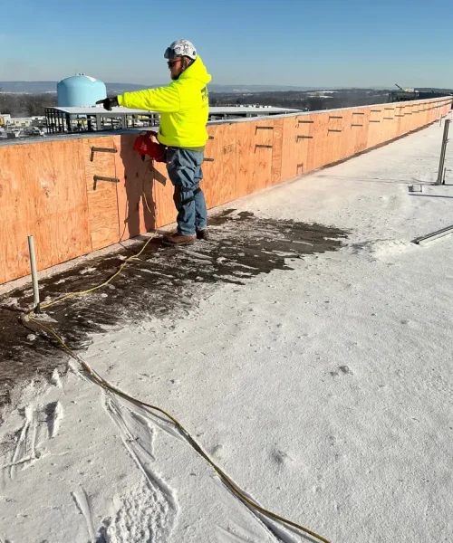 RTG Solutions commercial roofer fastening plywood sheathing to a long parapet wall on the Hershey Pennsylvania State Police building during new roof construction