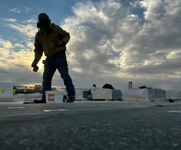 RTG roofer in cold weather gear working on the new Hershey Pennsylvania State Police building roof with bundled insulation and dramatic clouds in the background