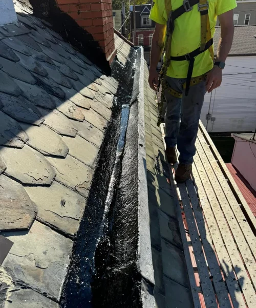 Contractor performing slate roof and gutter repairs, sealing valleys to improve water drainage and extend roof life in Pennsylvania.
